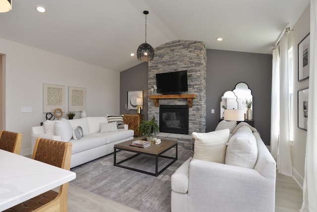 living room featuring lofted ceiling, light hardwood / wood-style flooring, and a stone fireplace