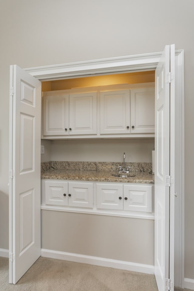 interior space featuring white cabinetry, sink, light colored carpet, and light stone countertops