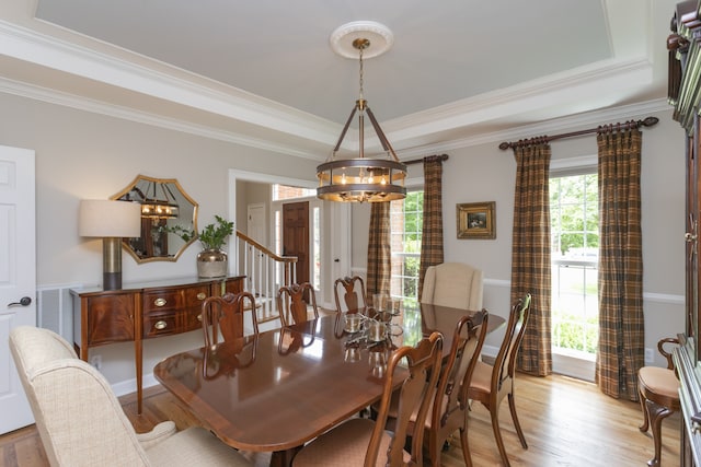 dining space with crown molding, an inviting chandelier, a tray ceiling, and light wood-type flooring