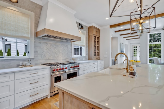 kitchen with custom range hood, light wood-type flooring, tasteful backsplash, a chandelier, and double oven range