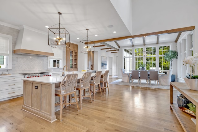 kitchen featuring hanging light fixtures, custom range hood, light hardwood / wood-style flooring, and white cabinetry