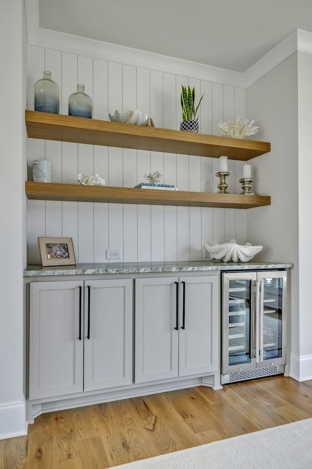 bar with light hardwood / wood-style floors, white cabinets, wine cooler, light stone countertops, and ornamental molding