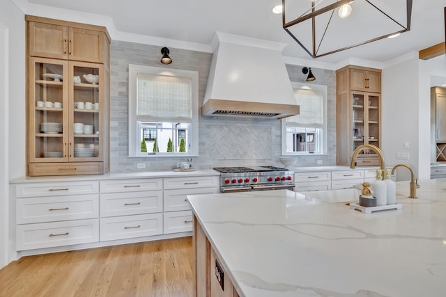 kitchen with backsplash, custom range hood, range with two ovens, and light stone counters