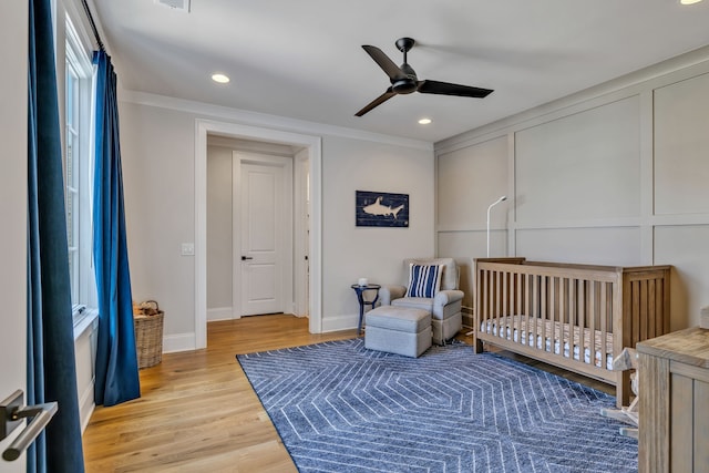 bedroom with a nursery area, crown molding, light hardwood / wood-style floors, and ceiling fan