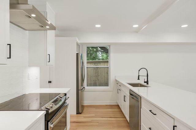 kitchen featuring white cabinetry, sink, light wood-type flooring, stainless steel appliances, and wall chimney range hood