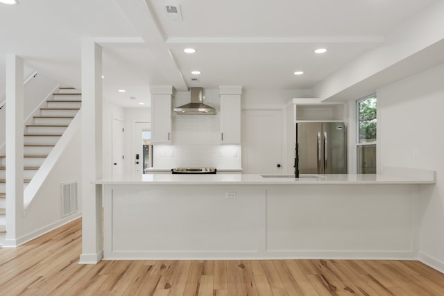 kitchen with appliances with stainless steel finishes, white cabinets, light wood-type flooring, backsplash, and wall chimney range hood