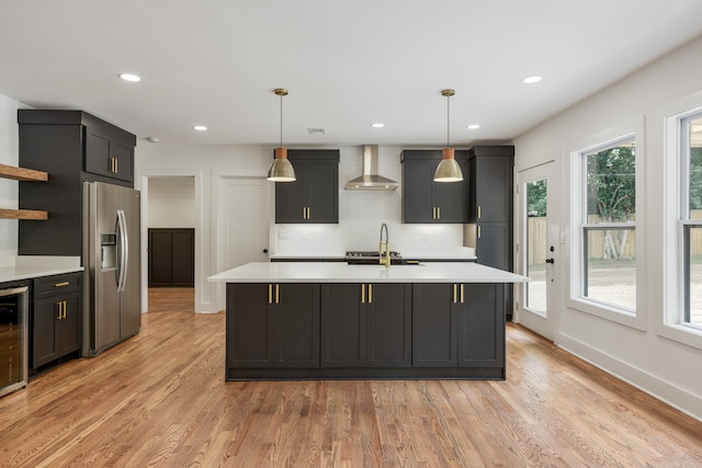 kitchen featuring light hardwood / wood-style flooring, pendant lighting, wall chimney exhaust hood, and stainless steel fridge