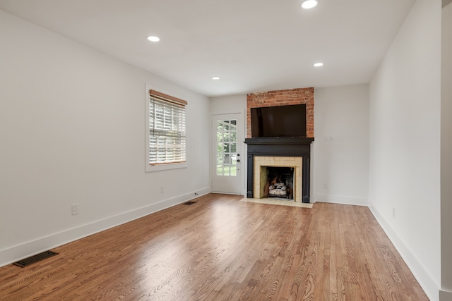 unfurnished living room with brick wall, light wood-type flooring, and a fireplace