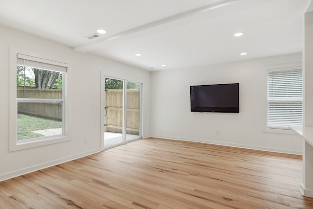 unfurnished room with a wealth of natural light, beamed ceiling, and light hardwood / wood-style floors