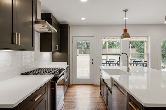 kitchen featuring appliances with stainless steel finishes, tasteful backsplash, a center island with sink, light wood-type flooring, and pendant lighting