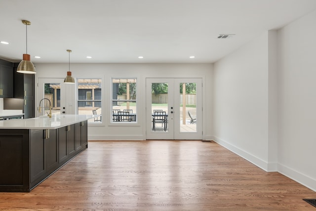 kitchen with an island with sink, pendant lighting, french doors, light hardwood / wood-style flooring, and sink