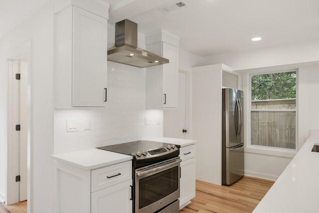 kitchen with white cabinets, appliances with stainless steel finishes, wall chimney exhaust hood, and light hardwood / wood-style flooring