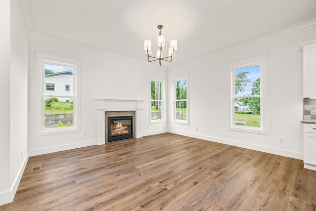 unfurnished living room with a chandelier, ornamental molding, wood-type flooring, and a wealth of natural light