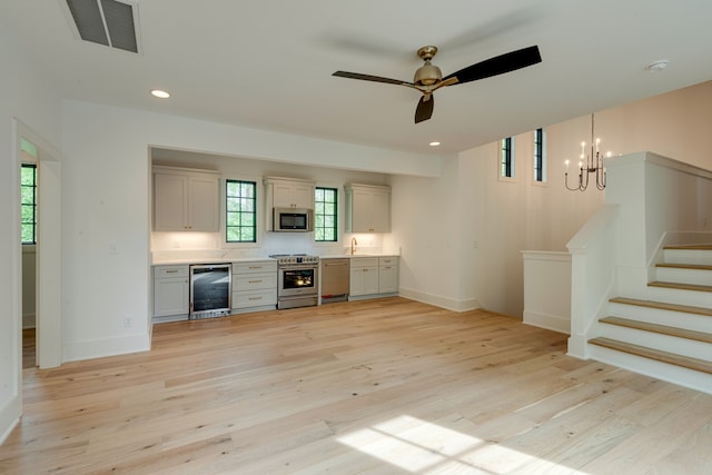 kitchen with hanging light fixtures, ceiling fan with notable chandelier, light wood-type flooring, wine cooler, and stainless steel appliances