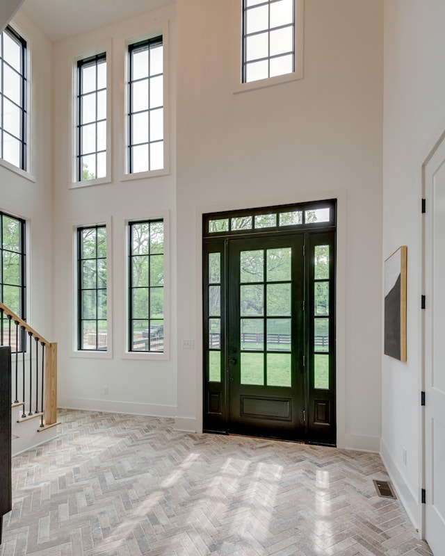 entryway featuring a towering ceiling, light parquet flooring, and a healthy amount of sunlight