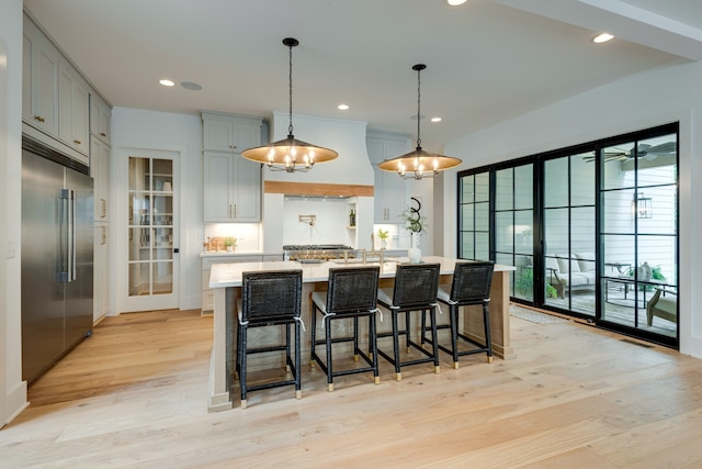 kitchen featuring a breakfast bar, stainless steel built in fridge, light hardwood / wood-style floors, and a kitchen island with sink