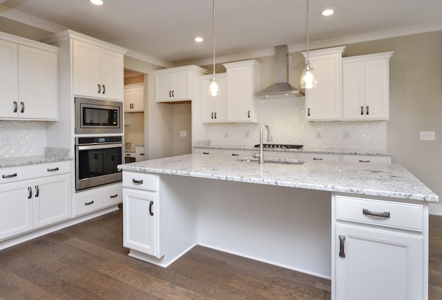 kitchen with stainless steel appliances, a center island with sink, wall chimney exhaust hood, white cabinets, and backsplash