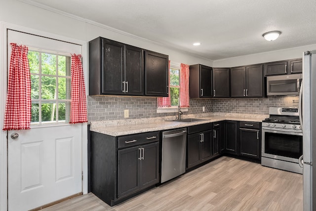 kitchen featuring appliances with stainless steel finishes, tasteful backsplash, light hardwood / wood-style floors, light stone countertops, and sink