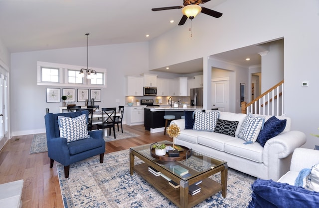 living room with high vaulted ceiling, ceiling fan with notable chandelier, sink, and light hardwood / wood-style floors