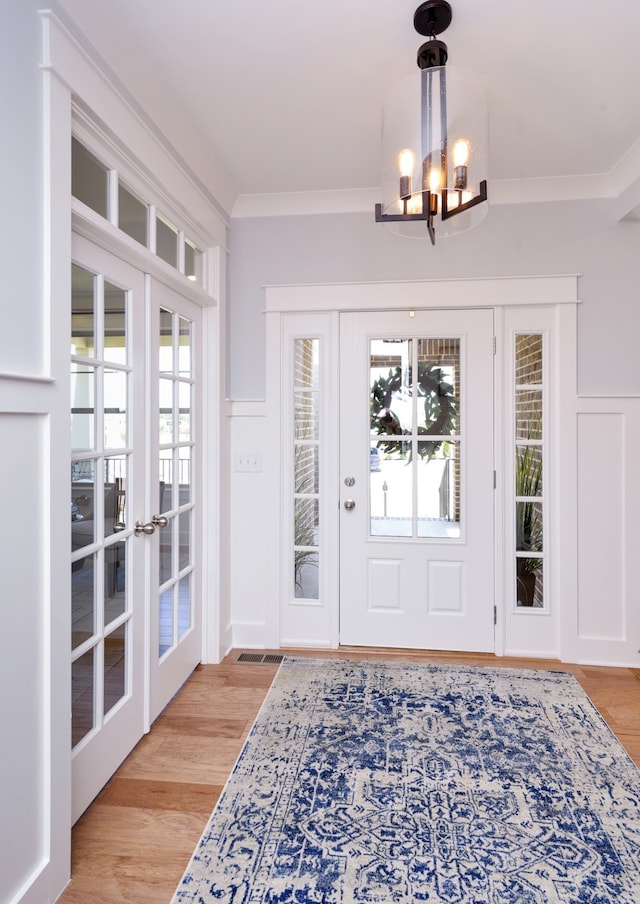 foyer with a notable chandelier, ornamental molding, light hardwood / wood-style floors, and french doors