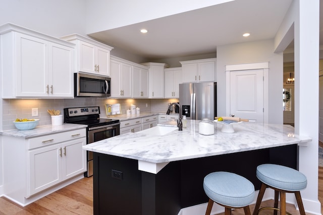 kitchen featuring appliances with stainless steel finishes, backsplash, light hardwood / wood-style floors, and white cabinets