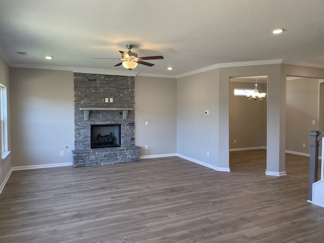 unfurnished living room with crown molding, dark wood-type flooring, ceiling fan with notable chandelier, and a stone fireplace