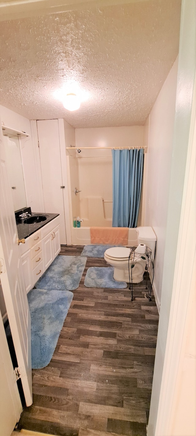 full bathroom featuring toilet, a textured ceiling, vanity, shower / bath combination with curtain, and wood-type flooring