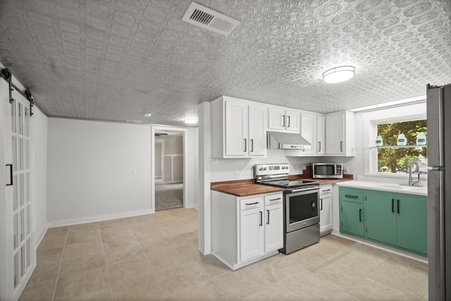 kitchen featuring a barn door, green cabinets, white cabinets, and appliances with stainless steel finishes