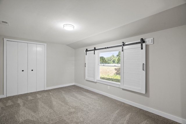 unfurnished bedroom with lofted ceiling, a closet, carpet, and a barn door