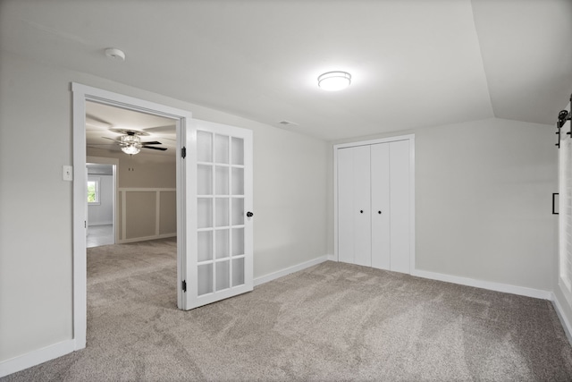 spare room with a barn door, ceiling fan, vaulted ceiling, and light colored carpet