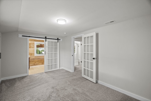 carpeted empty room with a barn door, french doors, and vaulted ceiling