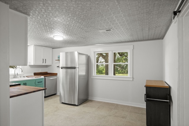 kitchen featuring white cabinetry, wood counters, light tile floors, stainless steel appliances, and sink