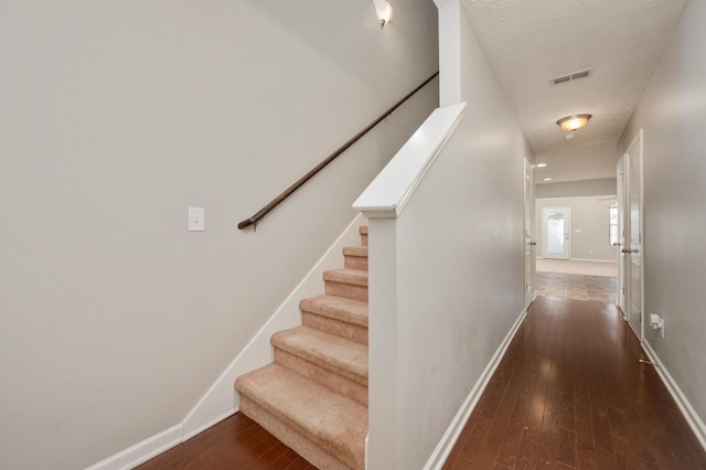 stairs featuring a textured ceiling and dark wood-type flooring