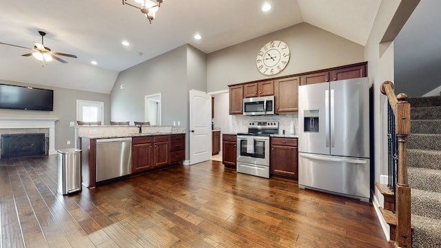 kitchen featuring ceiling fan, light stone counters, dark hardwood / wood-style flooring, stainless steel appliances, and a fireplace