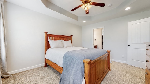 bedroom featuring ceiling fan, ensuite bath, a raised ceiling, and light colored carpet