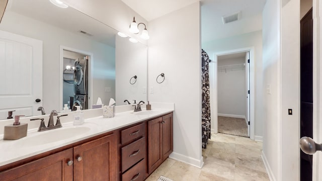 bathroom with dual bowl vanity, tile flooring, and stacked washing maching and dryer