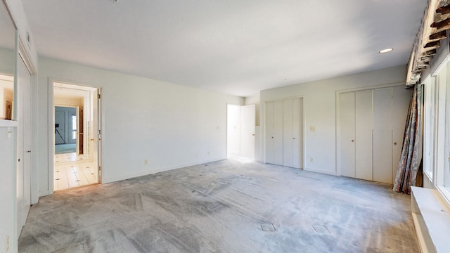 unfurnished bedroom featuring light colored carpet, multiple closets, and ensuite bath