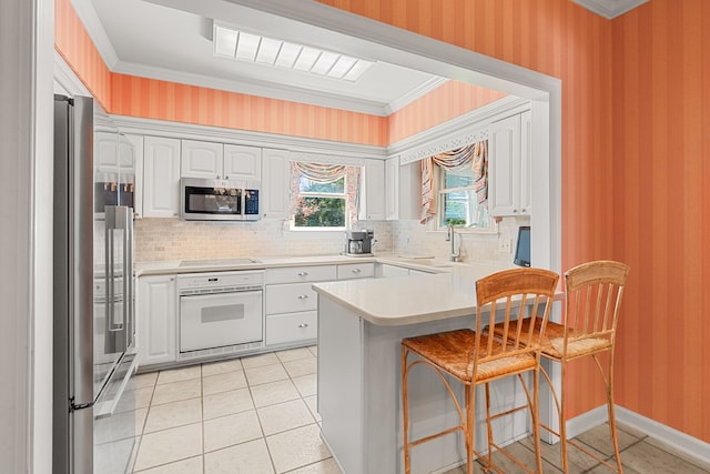 kitchen with stainless steel appliances, a kitchen breakfast bar, tasteful backsplash, ornamental molding, and white cabinetry