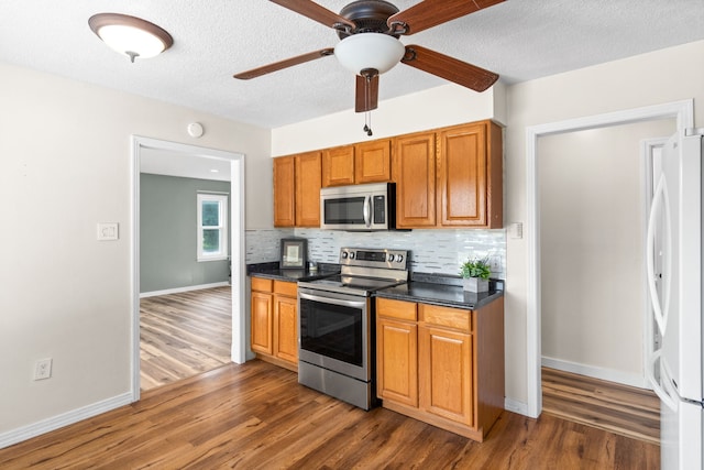 kitchen featuring dark hardwood / wood-style floors, ceiling fan, appliances with stainless steel finishes, and tasteful backsplash