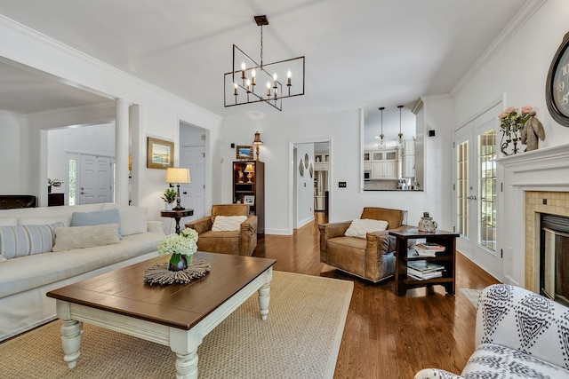 living room with a tiled fireplace, crown molding, dark hardwood / wood-style flooring, and an inviting chandelier