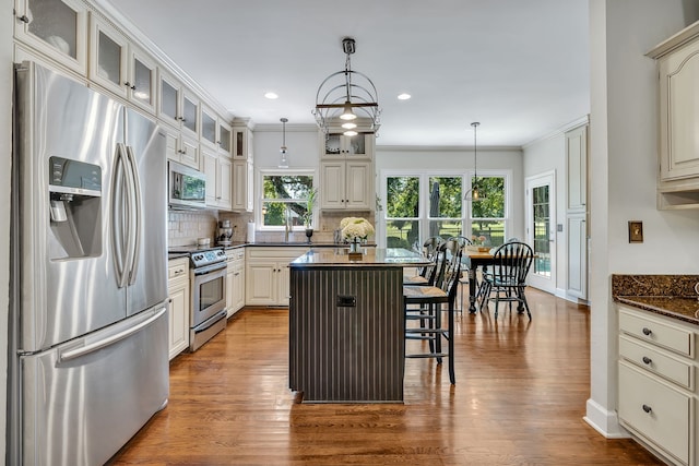 kitchen featuring stainless steel appliances, a center island, tasteful backsplash, wood-type flooring, and hanging light fixtures