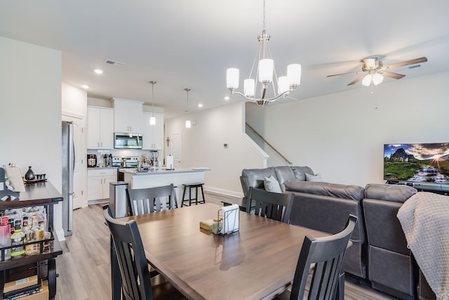 dining room with ceiling fan with notable chandelier and light hardwood / wood-style flooring