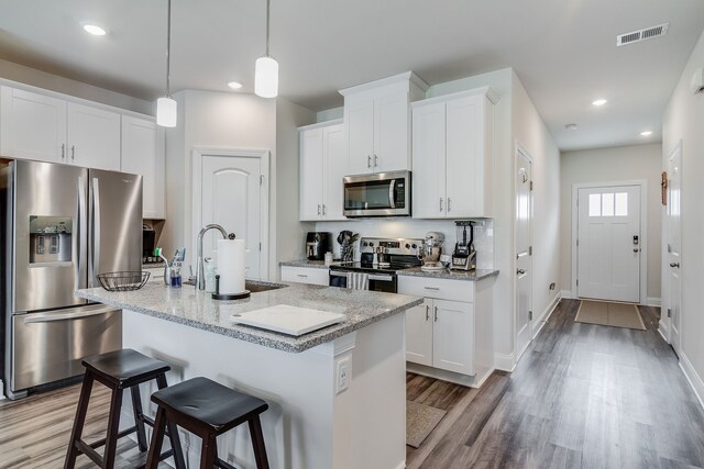 kitchen with light hardwood / wood-style floors, stainless steel appliances, white cabinets, a kitchen island with sink, and sink