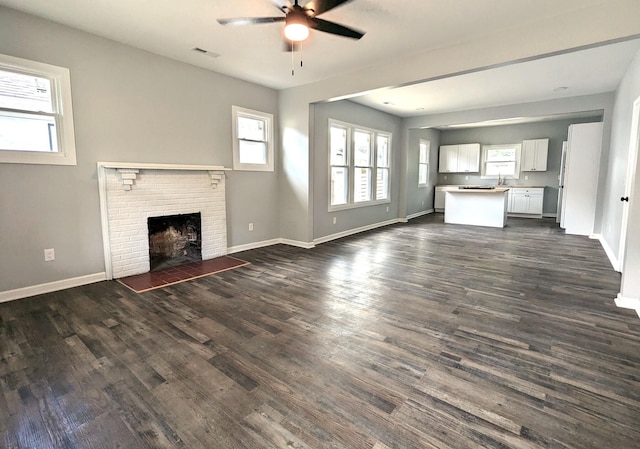 unfurnished living room featuring a fireplace, ceiling fan, sink, and dark hardwood / wood-style flooring