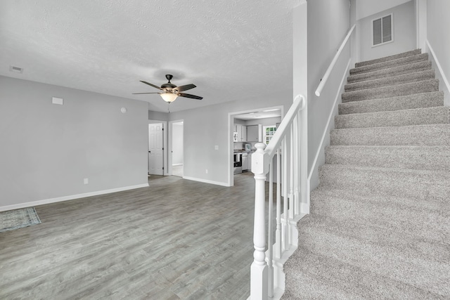 staircase with a textured ceiling, ceiling fan, and dark hardwood / wood-style flooring