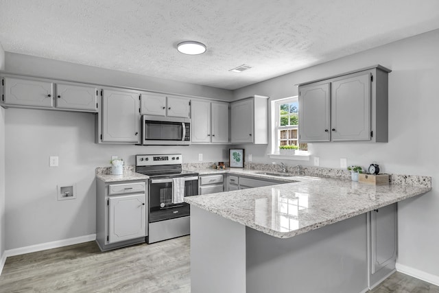 kitchen with gray cabinets, light hardwood / wood-style floors, kitchen peninsula, and appliances with stainless steel finishes