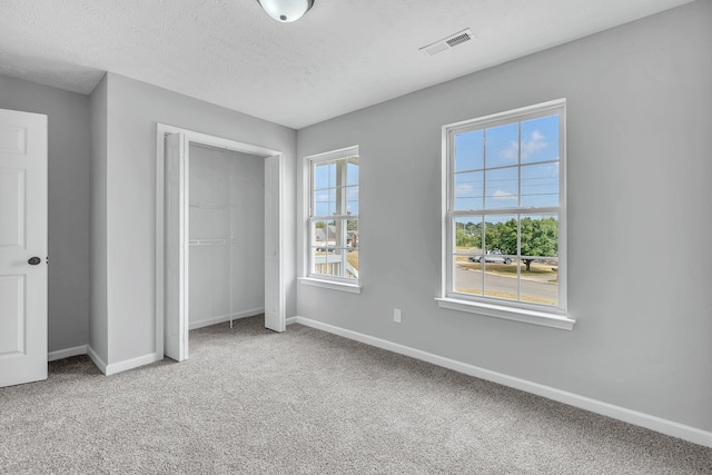 unfurnished bedroom with a closet, a textured ceiling, and light colored carpet