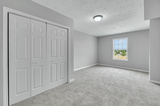 unfurnished bedroom featuring a textured ceiling, light colored carpet, and a closet