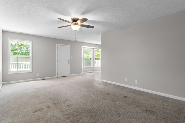 carpeted spare room with a textured ceiling, ceiling fan, and a healthy amount of sunlight