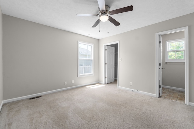 unfurnished bedroom with light colored carpet, a walk in closet, and ceiling fan